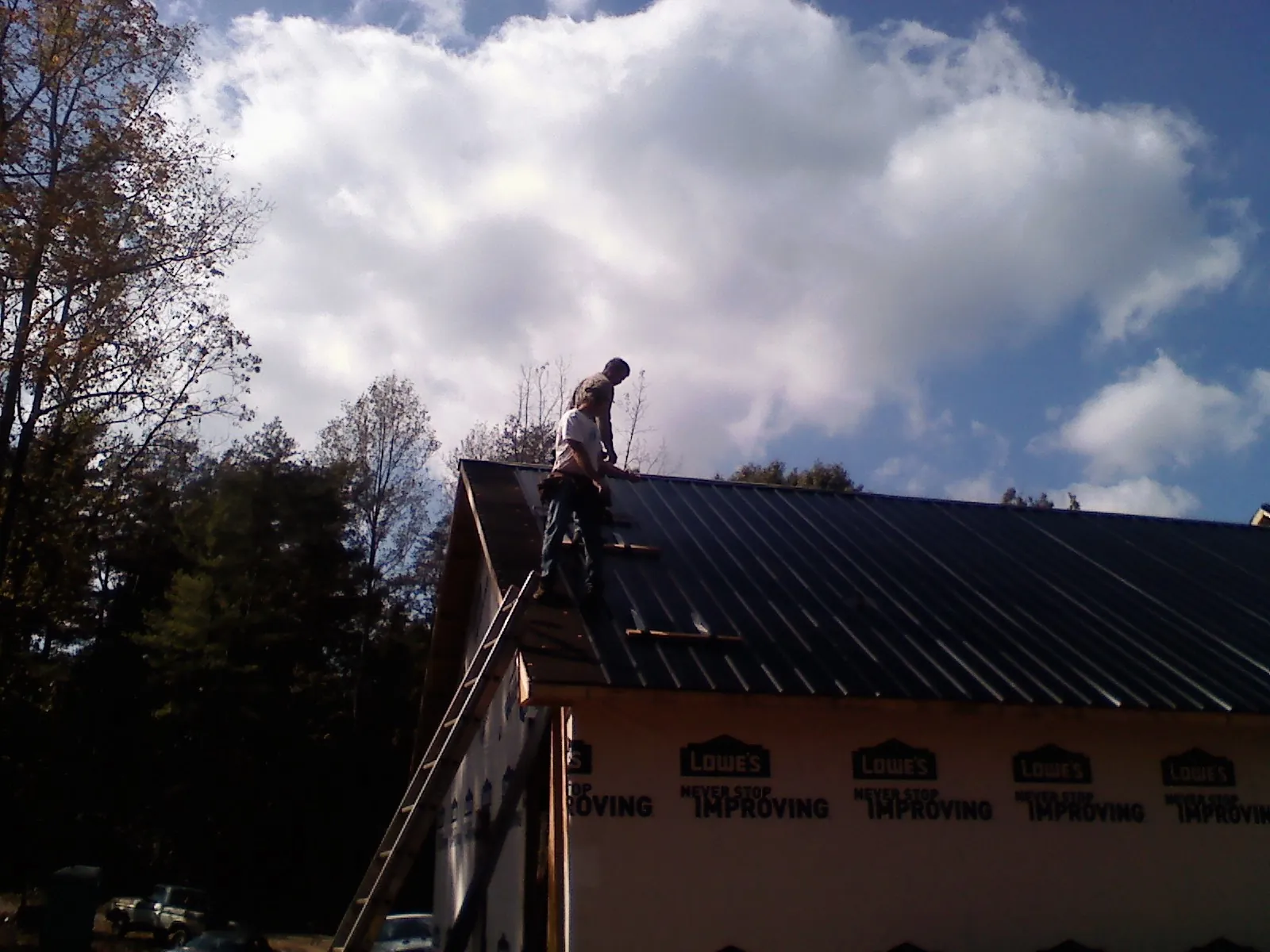 Roofer fastening dark metal panels high against a cloudy sky, from a Roof Inspection job in Effingham