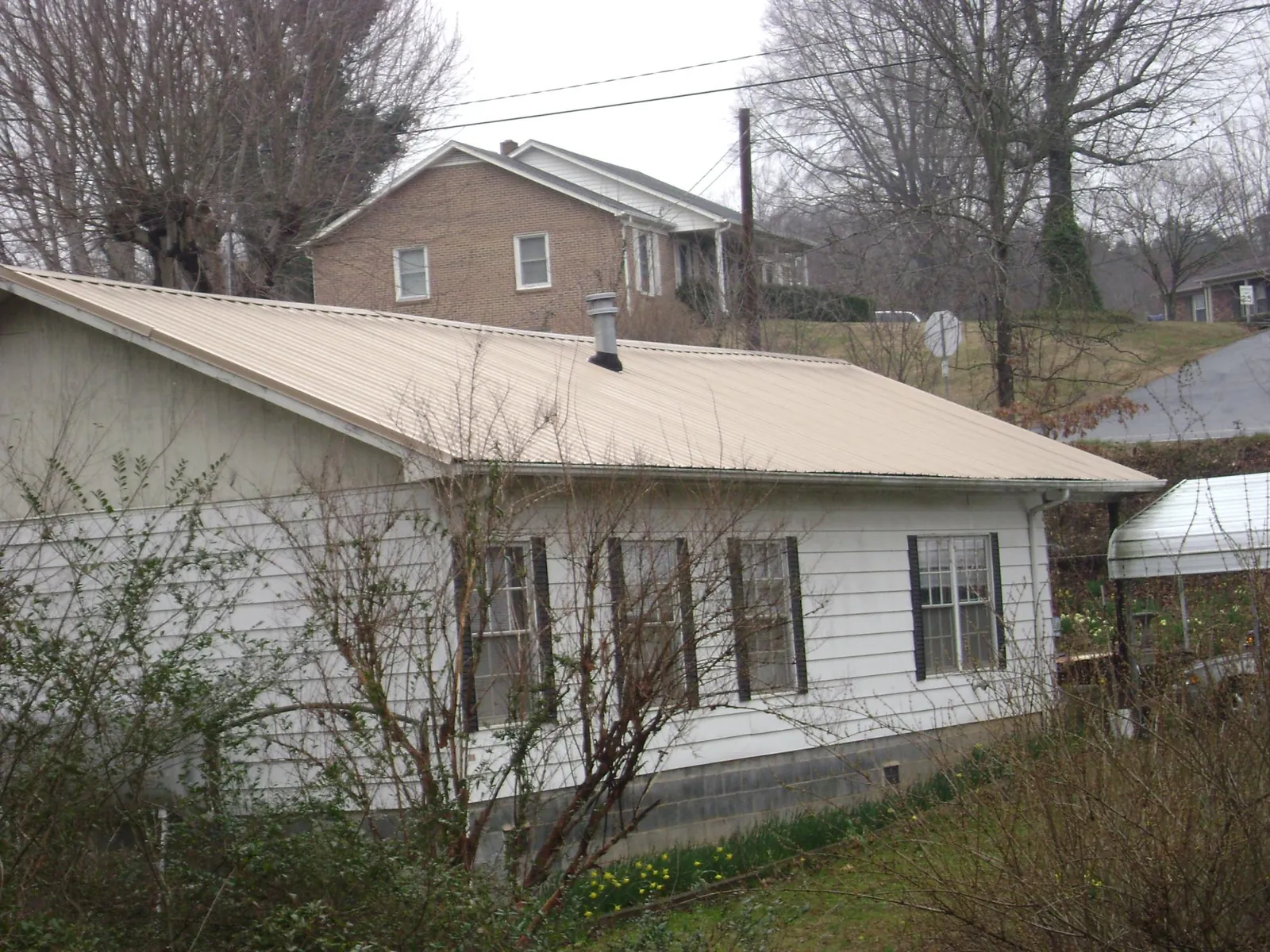 Tan metal roof on a white sided house set into a hillside — Commercial Roofing by Roofing Brothers in Effingham